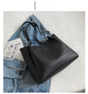 Detail of black tote bag featuring quilted texture and silver chain strap attachment