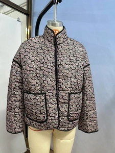 Detailed view of women's short quilted jacket with pink floral pattern and black piping