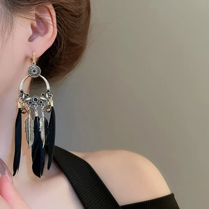 Détail de boucles d'oreilles bohèmes vintage avec plumes noires et dorées et pompons
