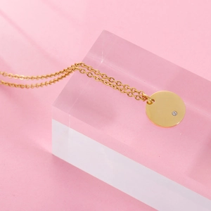 Polished gold circular necklace with small diamond on pink background with acrylic blocks