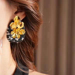 Detail of vintage gold flower embellishments on oval terrazzo resin earrings worn by model