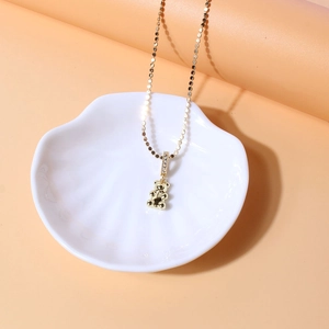 Detail of a 18K gold plated bear pendant necklace with zircon inlay on a shell tray