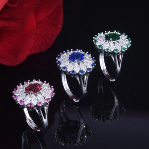 Detailed close-up of sapphire and ruby style sunflower rings on a black reflective surface