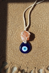 Detail of blue glass evil eye pendant and pink raw stone on woven cord