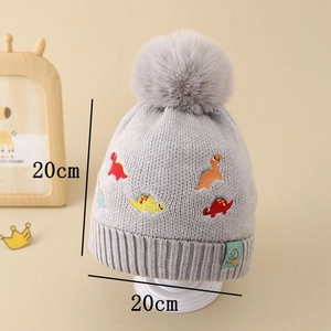 Détail d'un bonnet tricoté pour enfants avec broderie dinosaure et pompon gris