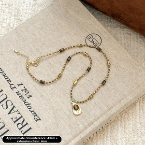 Détail d'un collier en pierre œil de tigre avec accents dorés sur fond crème