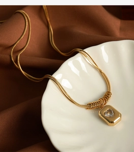 Detail of a double-layered gold snake chain with heart zircon pendant on a silk background