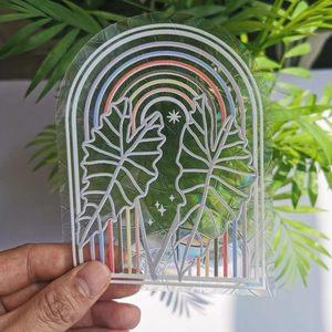 Macro view of holographic suncatcher sticker featuring rainbow and tropical leaf patterns
