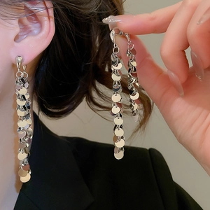 Détail macro de boucles d'oreilles longues à paillettes argentées et franges métal
