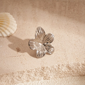 Close-up of a silver five-petal flower ear clip with metallic texture on stone