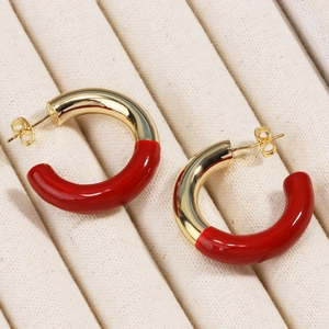 Gros plan de boucles d'oreilles créoles C émaillées rouges et dorées sur tapis beige