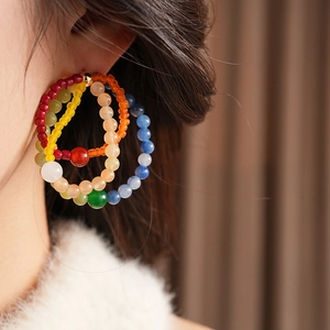 Detail shot of multi-layer colorful beaded hoop earrings on a model with gold metal studs