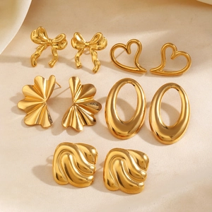 Set of four gold fashion earrings with bow, heart, and shell designs on soft fabric