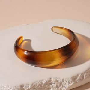 Detail of amber acrylic open bangle with gradient brown tones on a stone pedestal
