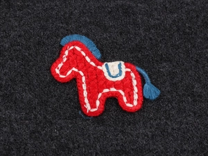 Detailed close-up of a red knitted horse embroidery patch on a navy knit cardigan