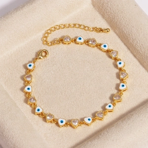 Close-up of golden heart chain bracelet with evil eye charms and sparkling zircon details