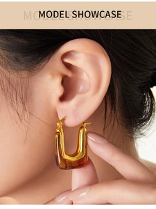 Close-up of a U-shaped gold metal and amber resin earring worn by a model in vintage style
