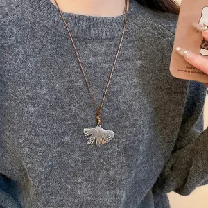 Ginkgo leaf pendant necklace in stainless steel with brown cord on a gray sweater