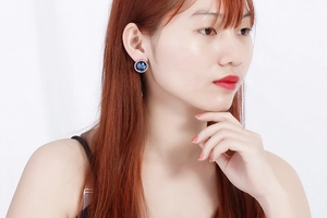 Close-up of a silver earring featuring a large round blue crystal with halo gems