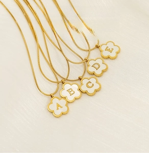 Macro detail of 18K gold-plated stainless steel clover pendants with A-E shell letters
