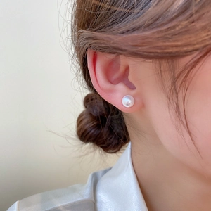 Close-up of a classic white pearl stud earring worn on a model's earlobe