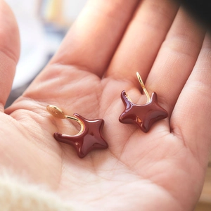 Macro shot of burgundy star-shaped earrings on a hand showing size and glossy finish