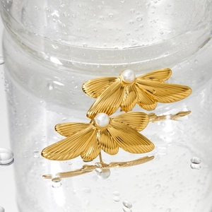 Elegant gold butterfly wing earrings with center pearl on a reflective water drop surface