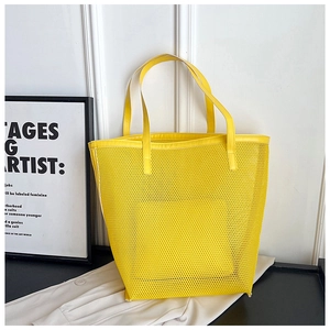 Detail of a bright yellow mesh tote bag with PVC trim on a dark surface and white background