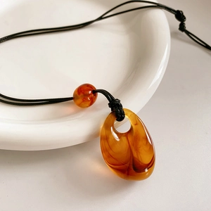 Detail of amber teardrop resin pendant on a black cord placed on white ceramic
