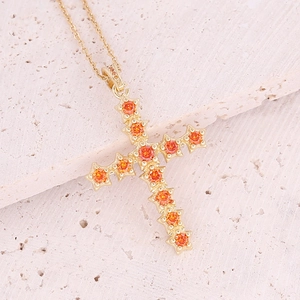 18K gold plated copper cross necklace with orange zircon stones on a stone surface