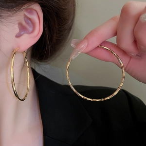 Detail of large gold hoop earrings with hammered texture worn with a dark suit