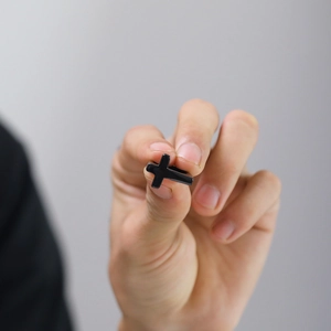 Detail of a glossy black stainless steel cross ring held to show its size and finish