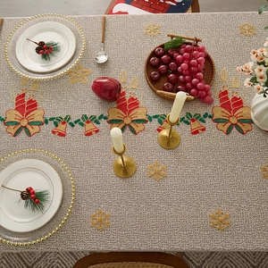 Detail of beige Christmas tablecloth with red bells, candles and snowflake lace pattern