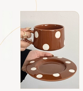 Détail d'un ensemble tasse et soucoupe en céramique marron avec motifs à pois blancs