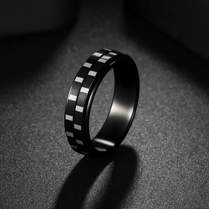 Rotating black titanium ring with checkerboard pattern on dark textured background