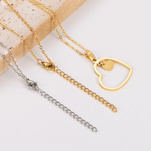 Close-up of gold and silver hollow heart necklaces displayed on a beige stone block