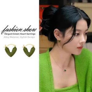 Detailed view of dark green heart enamel earrings with gold plating on model