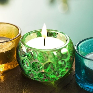 Macro shot of green polka dot glass candle holder with flame and soft bokeh background