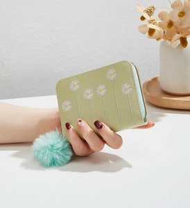 Close-up of light green plush purse with daisy embroidery and blue pompom pendant