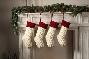 Detailansicht von vier gestrickten Weihnachtssocken mit rotem Rand am weißen Kamin