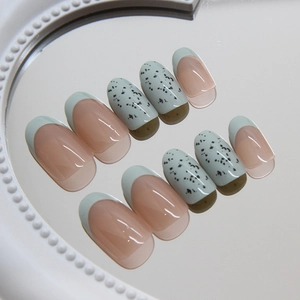 Mint green French press-on nails with black speckle patterns in oval shape