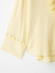 Macro detail of yellow chiffon top featuring pleated ruffles and woven cuff stitching