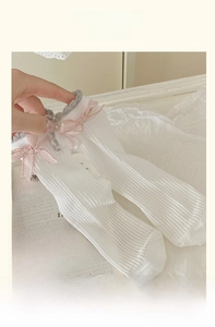 Dettaglio calzini in maglia bianca con bordo in pizzo grigio e fiocco di seta rosa