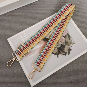 Macro detail of multi-color woven strap with geometric pattern and gold swivel hooks