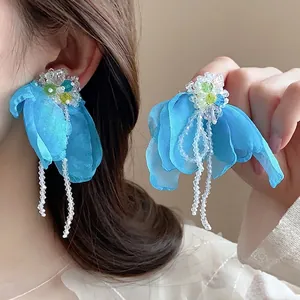 Macro detail of sky blue fabric flower earrings with crystal tassels on a soft background