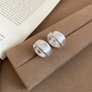 Close-up of matte brushed silver hoop earrings on a vintage brown jewelry stand