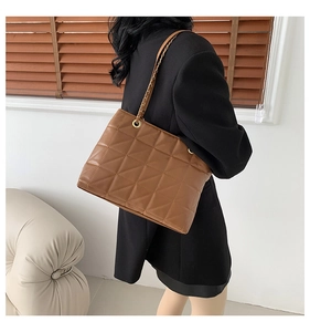 Detail of brown quilted tote bag with metallic chain strap worn over the shoulder