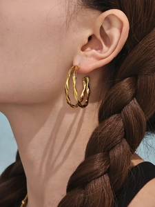 Détail de boucles d'oreilles créoles doubles torsadées dorées portées avec texture polie