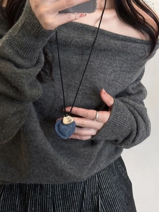 Close-up of denim heart pendant and gold tag on a black woven cord necklace