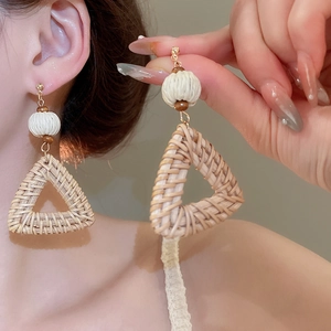 Detailed close-up of handmade triangular rattan earrings with wooden beads and resin accents